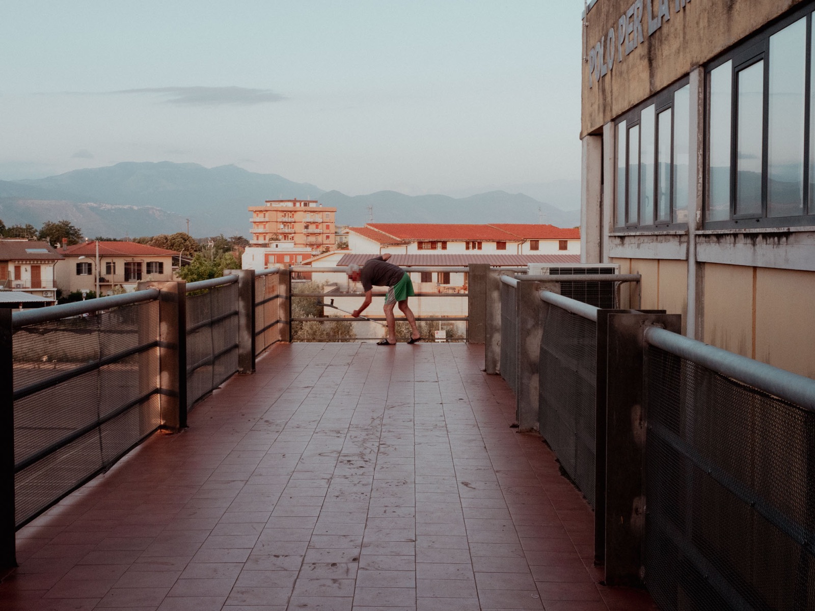 Un uomo spazza il ballatoio del dormitorio al tramonto, con le montagne sullo sfondo